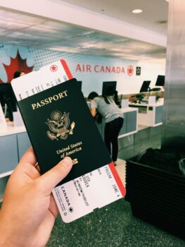 A smiling African worker holding a passport and luggage, with the Canadian flag in the background.